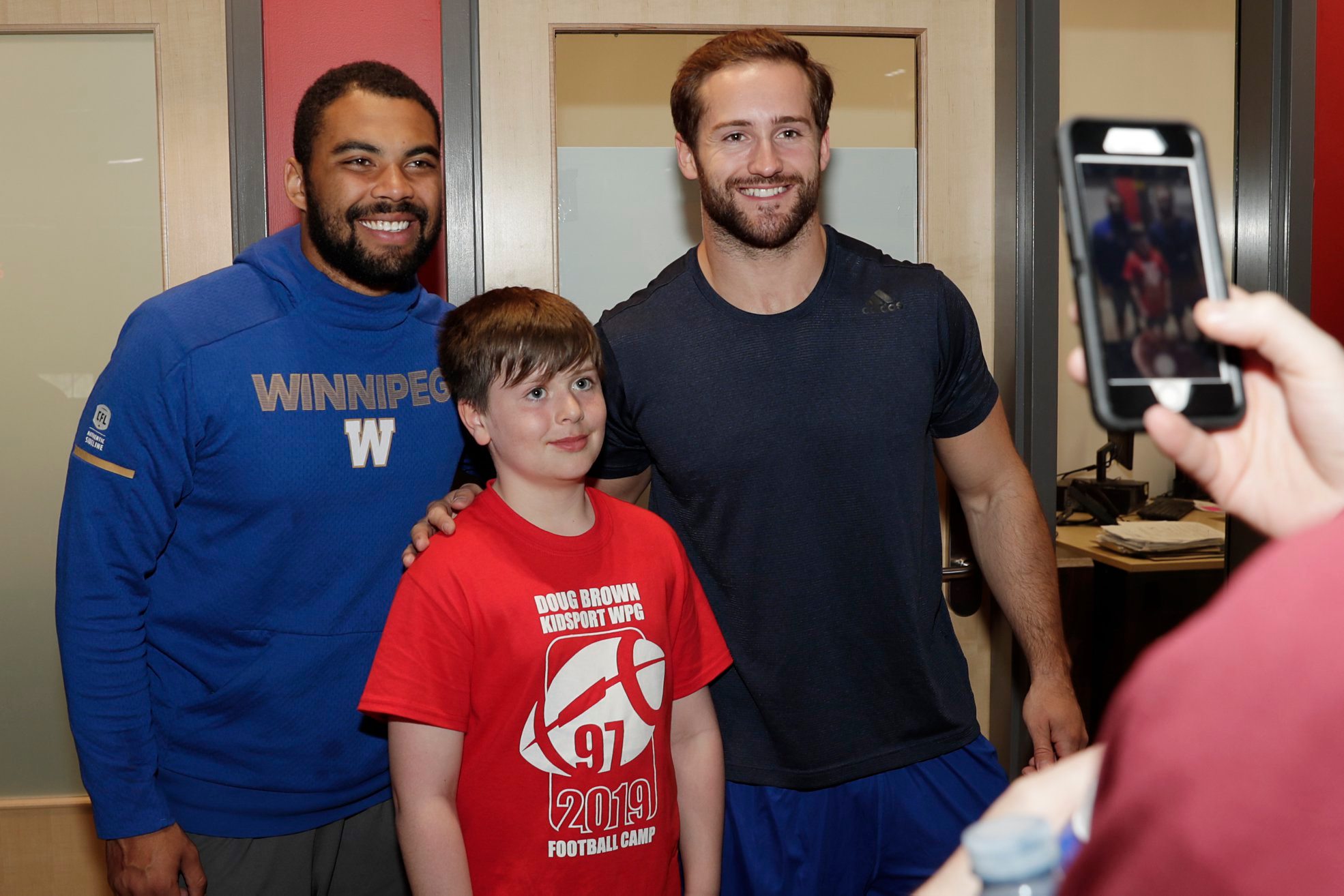 Ambassadors Nic Demski and Thomas Miles pose for a picture with a fan at the Doug Brown KidSPort Football camp